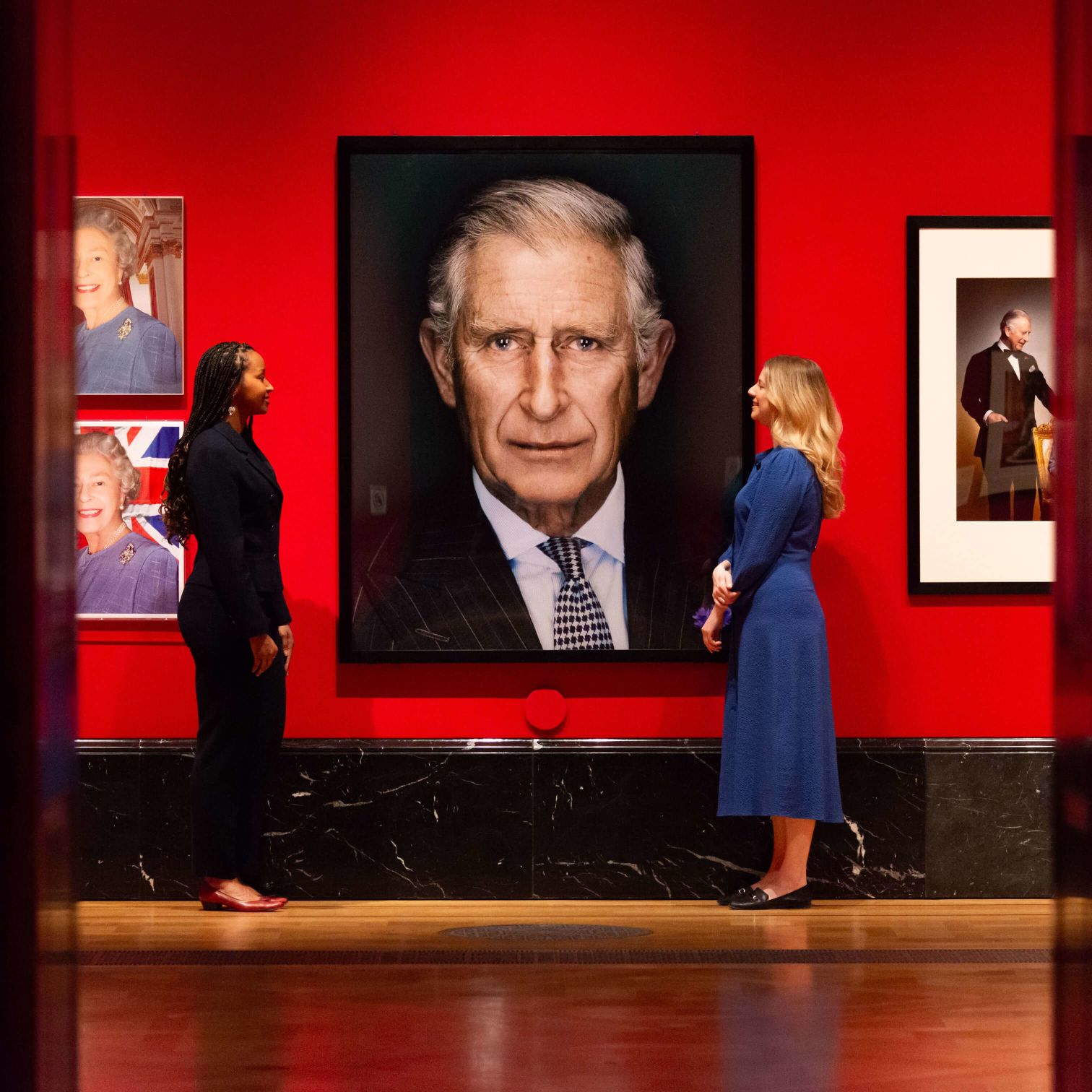 Prince Charles Standing Next To A Framed Picture Of A Man