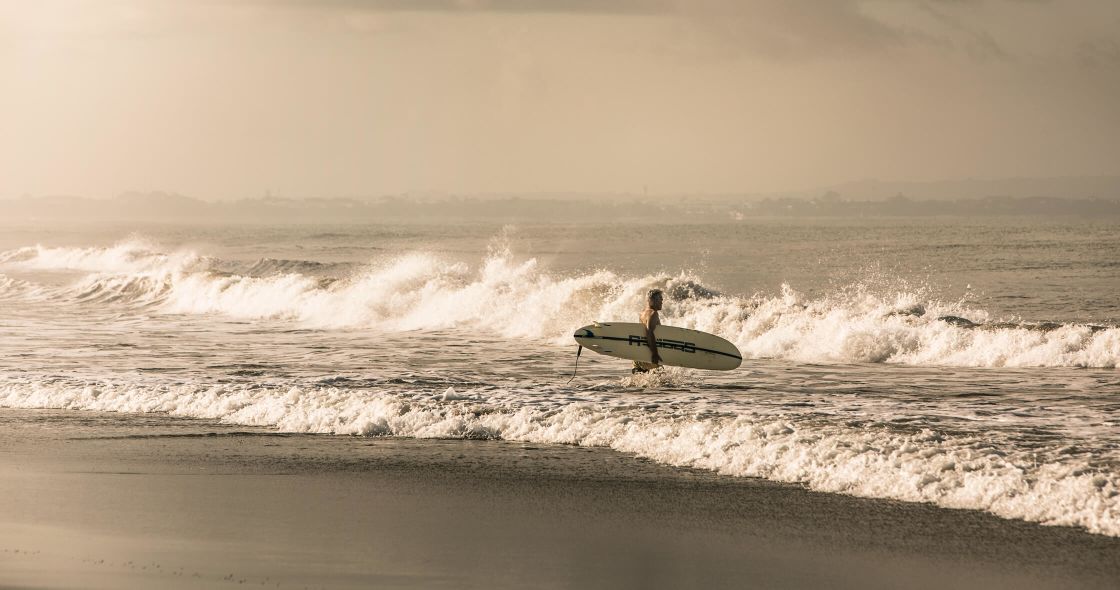 A Man Carrying A Surfboard On A Beach