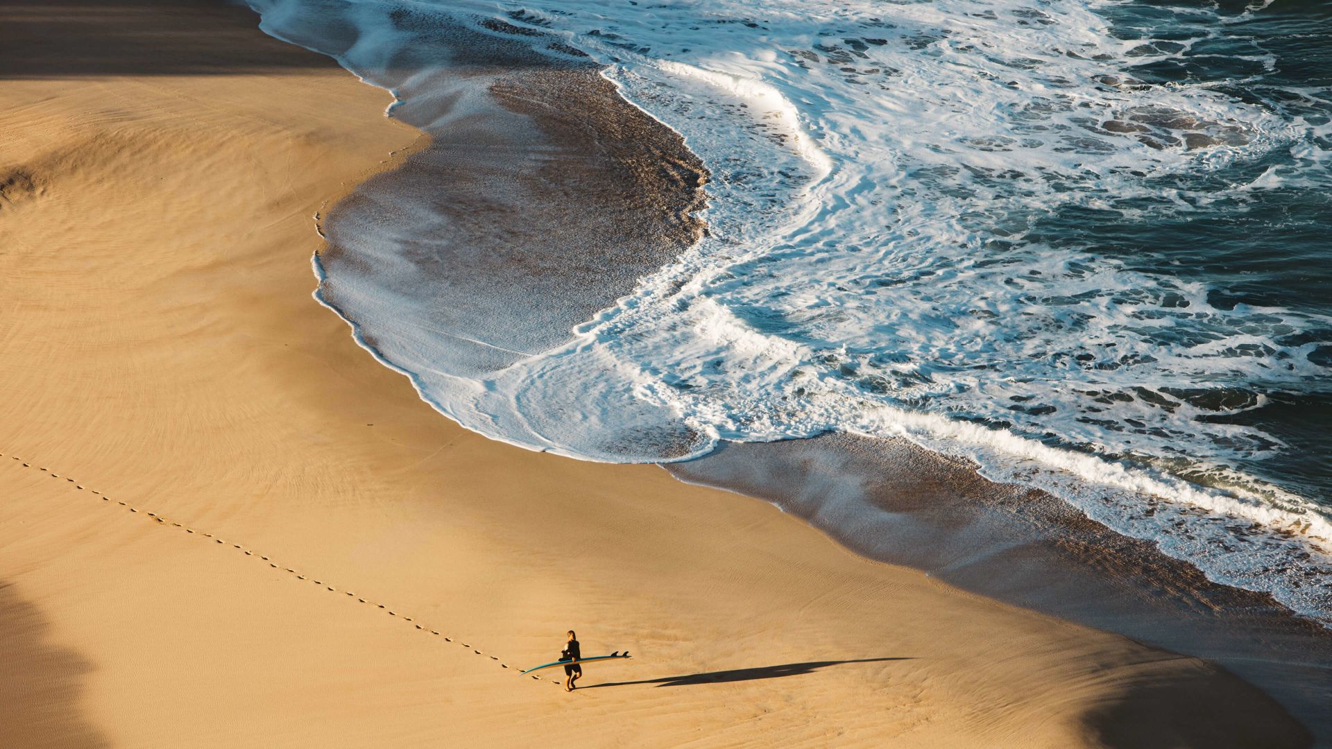 A Person Carrying A Surfboard On A Beach
