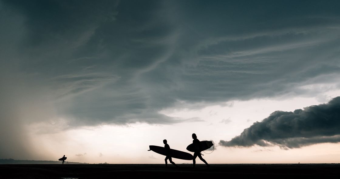 A Group Of Surfers Carrying Their Boards At Sunset