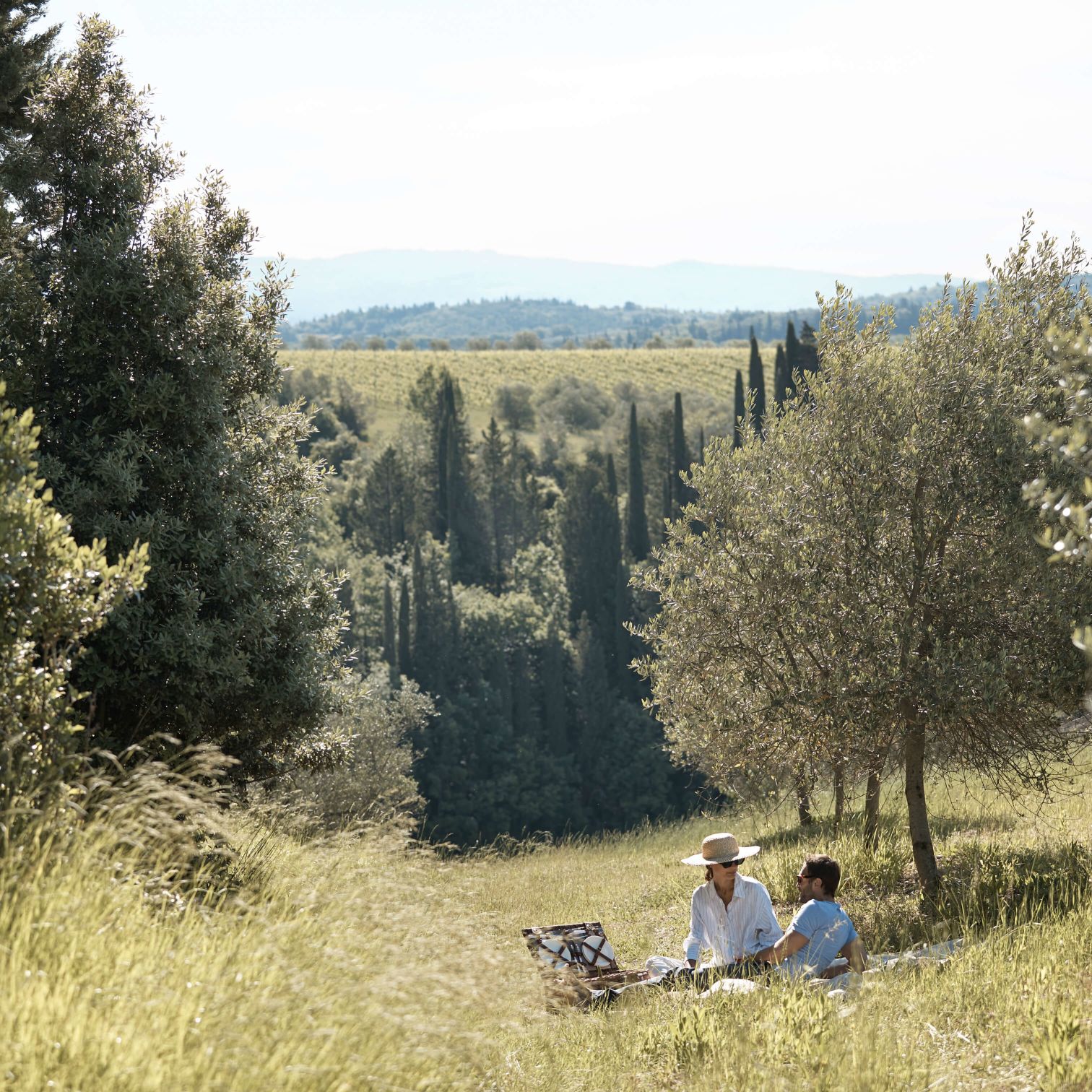 A Couple Of People Sitting On A Hill With Trees And A Field With A Fence And A Field