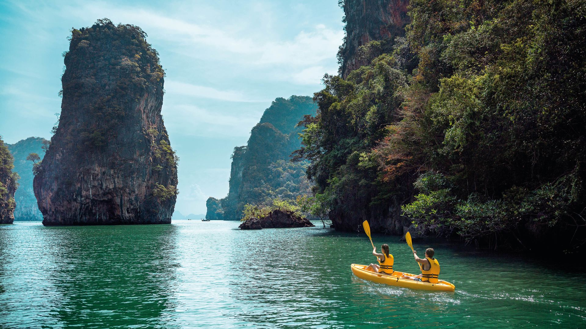 A Group Of People In A Canoe In A Body Of Water By A Large Rock Formation With Phi Phi Islands In The Background