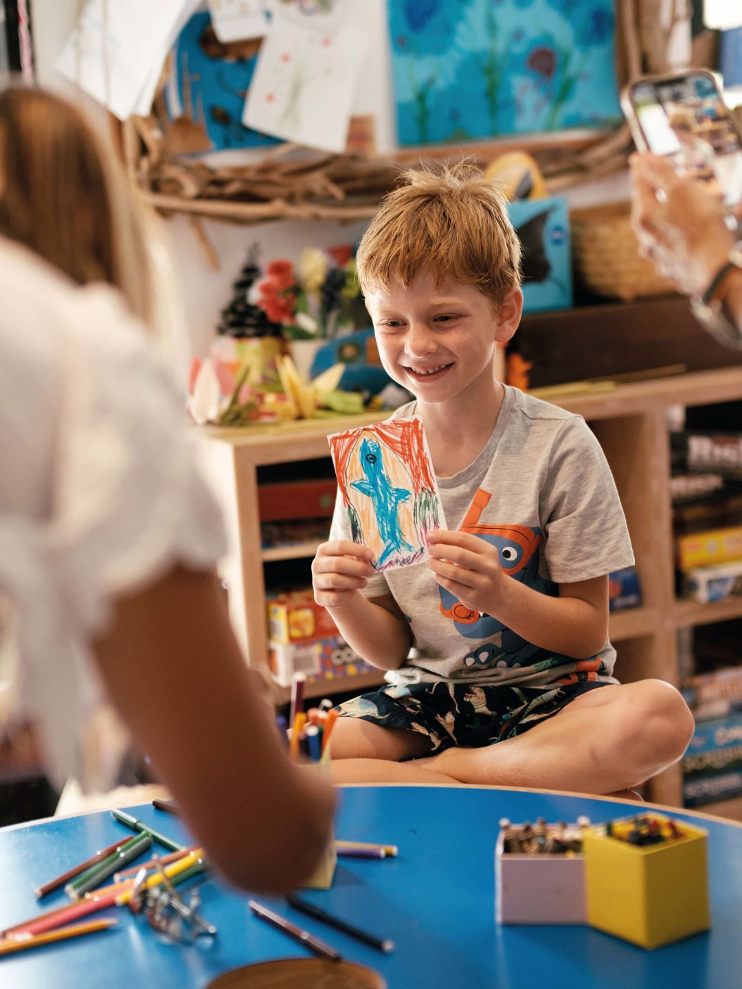 A Boy Sitting At A Table With Toys