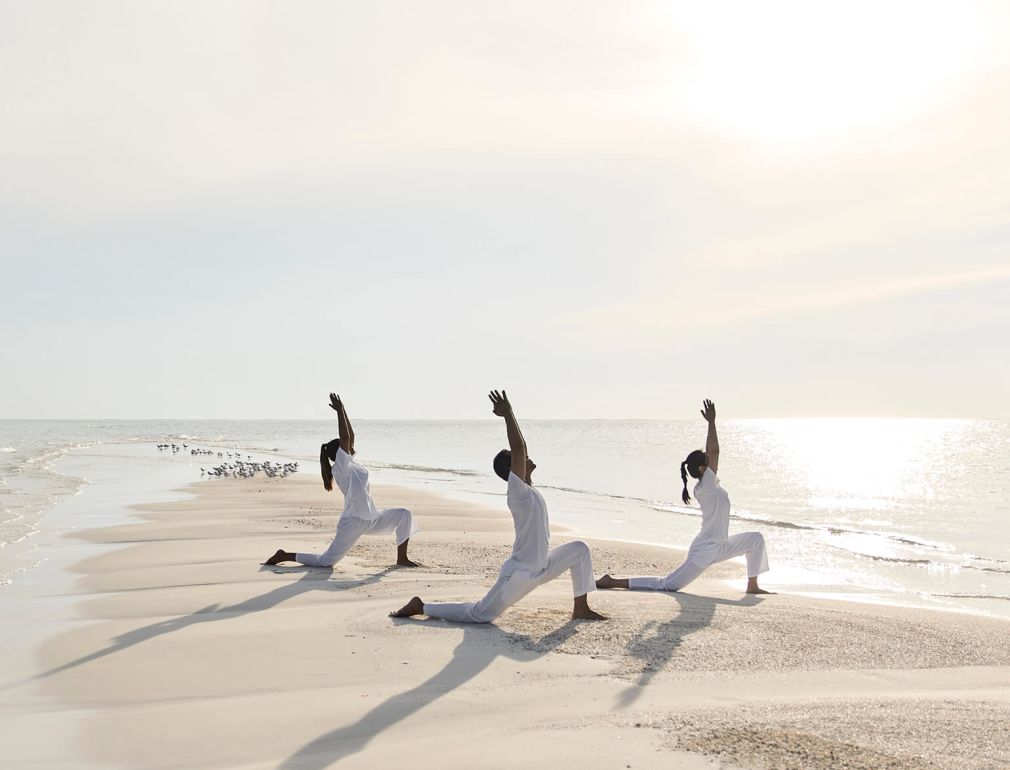 A Group Of People In White Outfits Jumping In The Air On A Beach