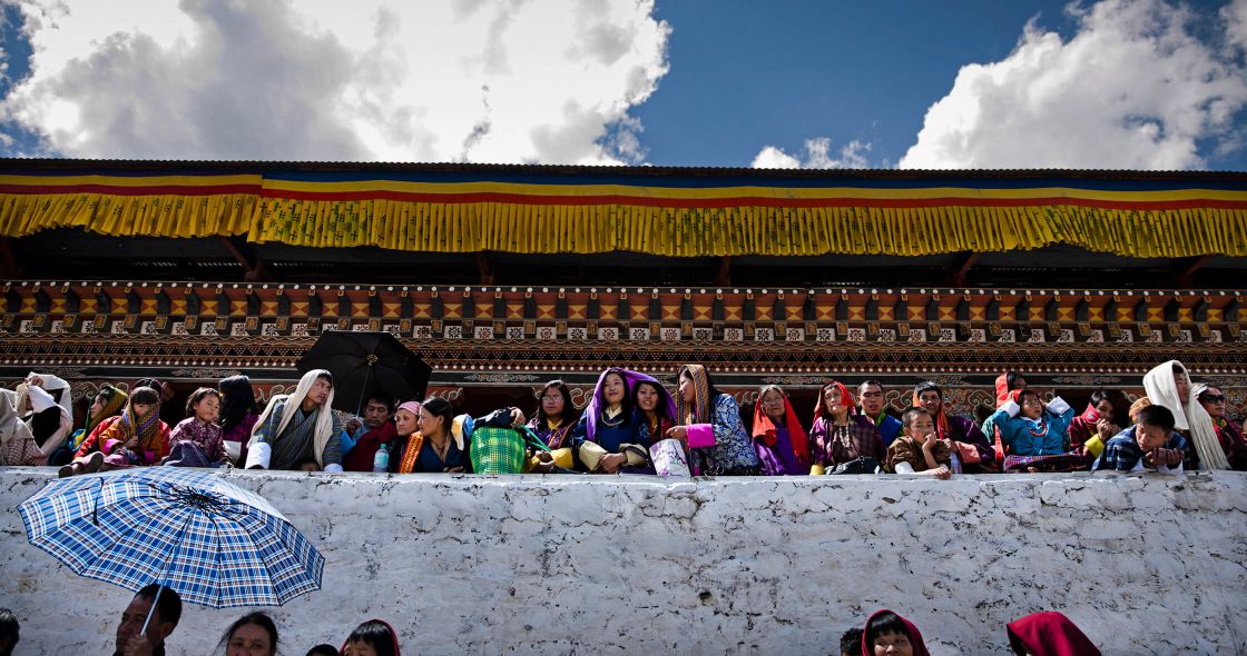 A Group Of People Sitting On A Ledge With Umbrellas