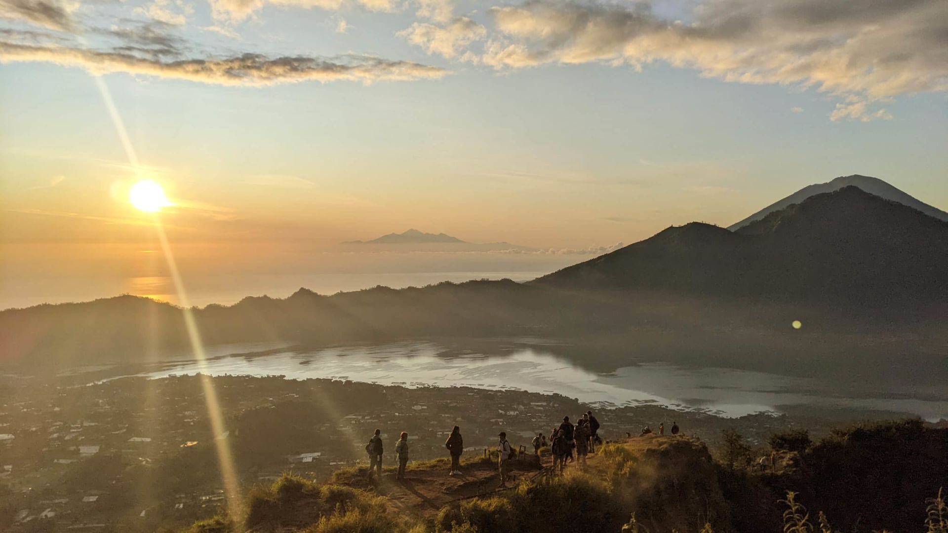 A Group Of People On A Mountain Top With A Body Of Water Below