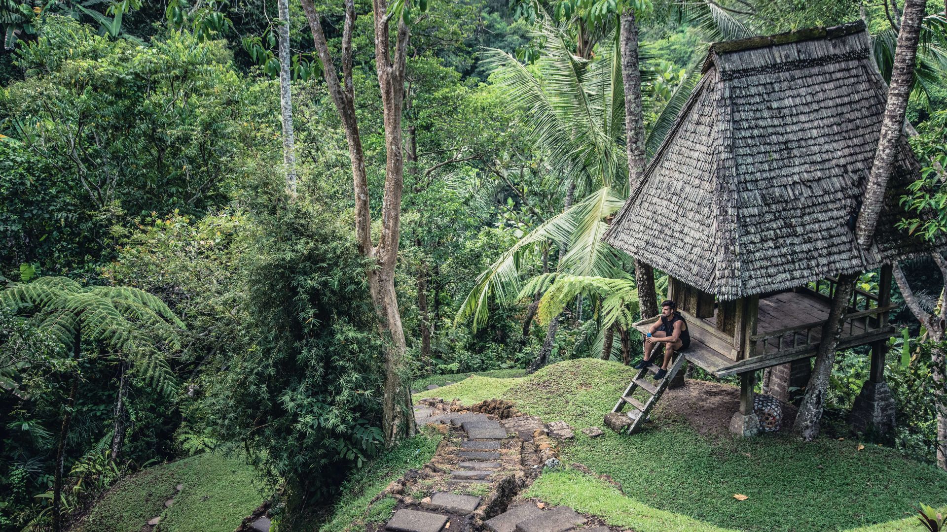 A Person Sitting On A Bench Next To A Hut In The Woods