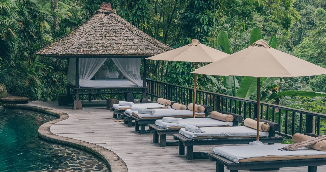 A Deck With Lounge Chairs And Umbrellas On It By A Body Of Water
