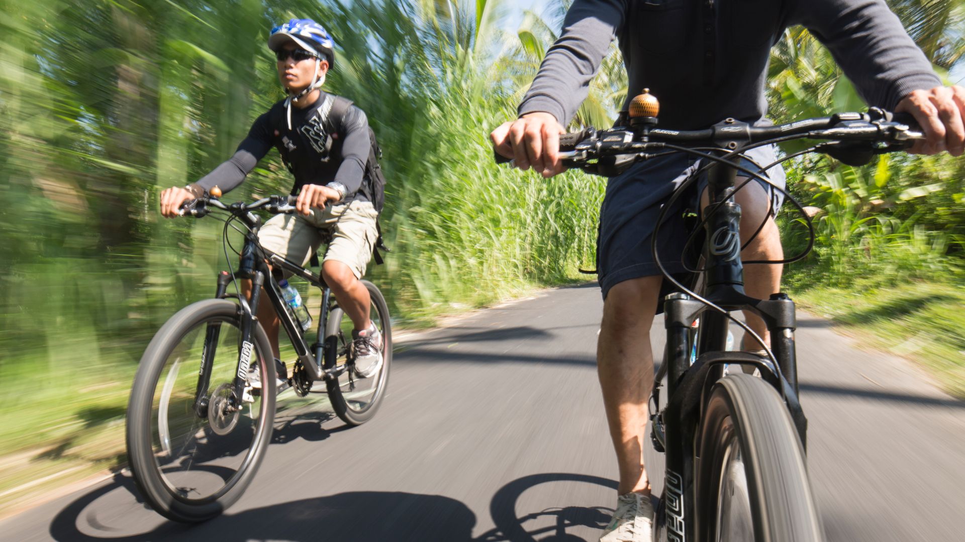 A Man Riding A Bike With Another Man On A Bike Behind Him