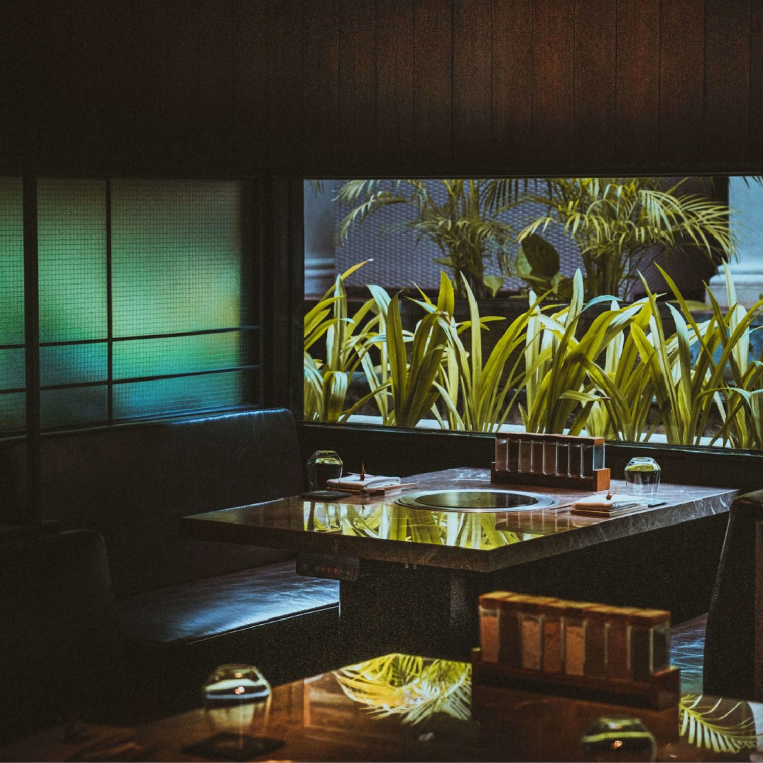 A Room With A Table And Chairs And A Window With Plants