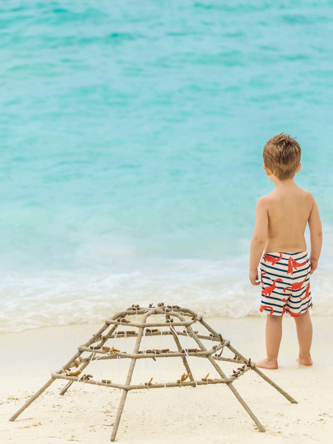 A Boy Standing Next To A Chair On A Beach
