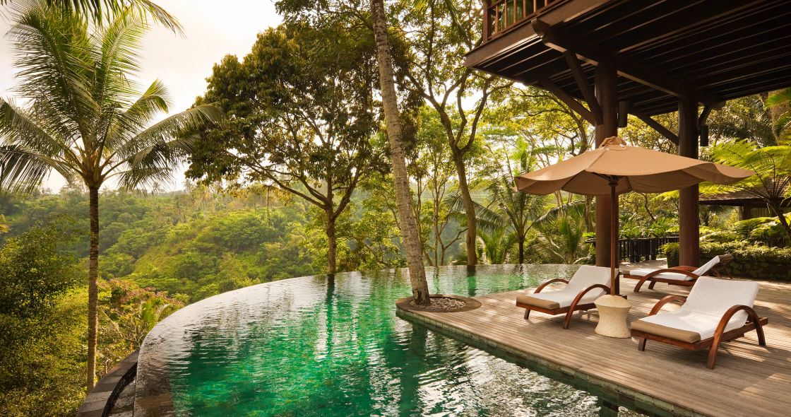 A Pool With Chairs And Umbrellas Next To A House