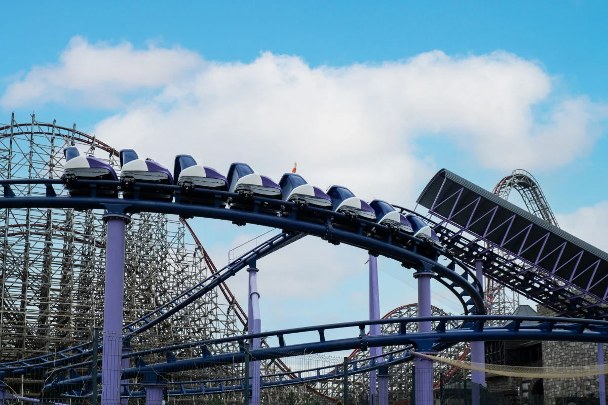 The picture shows a rollercoaster at the Energylandia theme park. You can see the track of the rollercoaster with the blue and white carriages. There are other parts of the rollercoaster in the background and the sky is blue with white clouds.